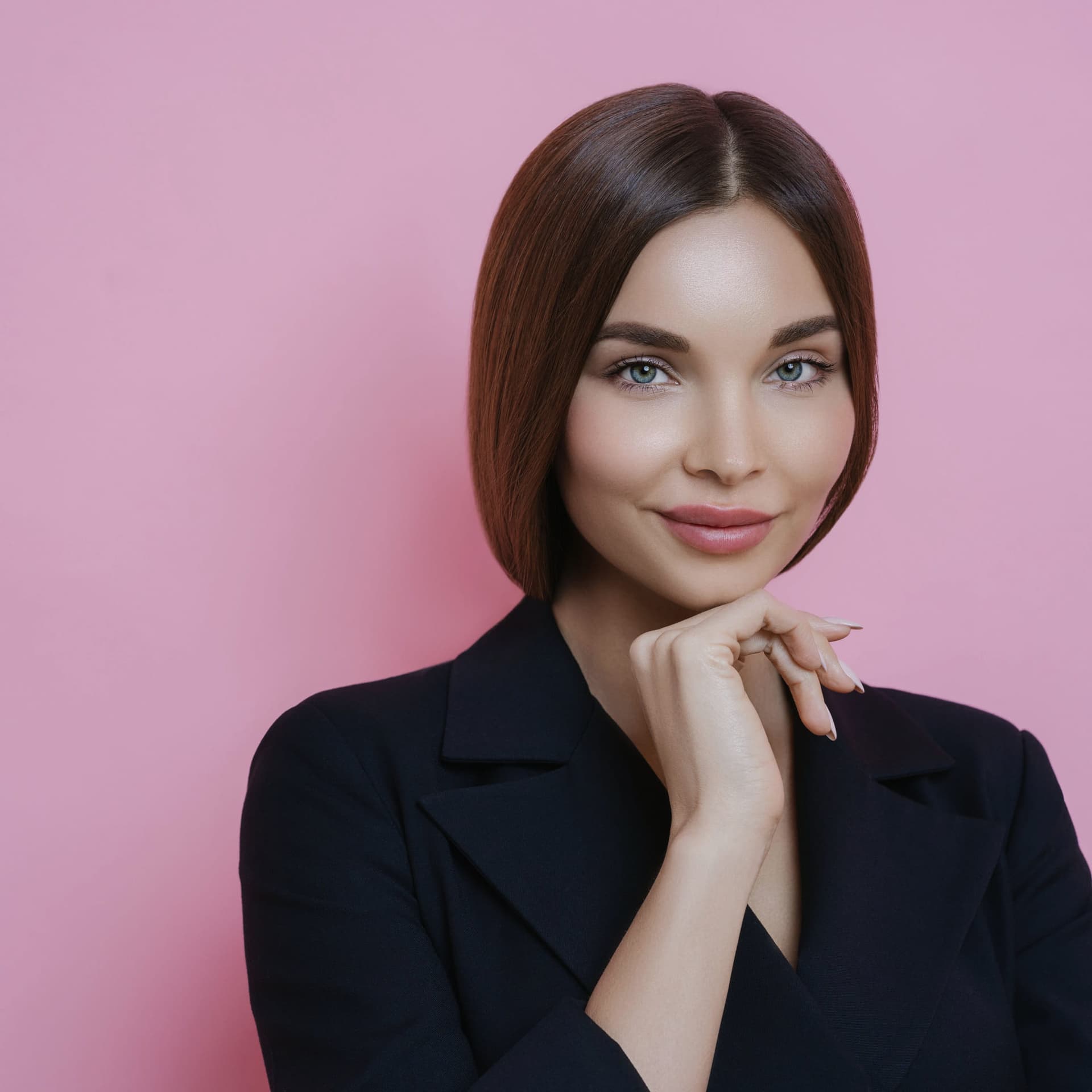 A model with a soft smile in a black blazer against a pink wall