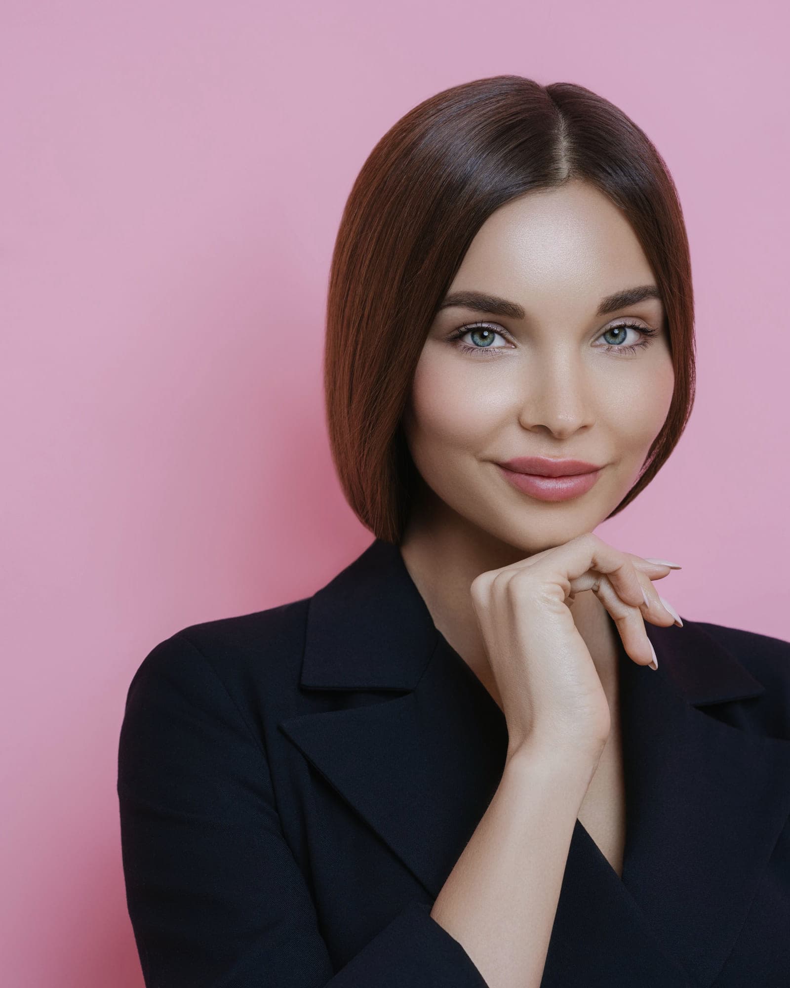 A model with a soft smile in a black blazer against a pink wall